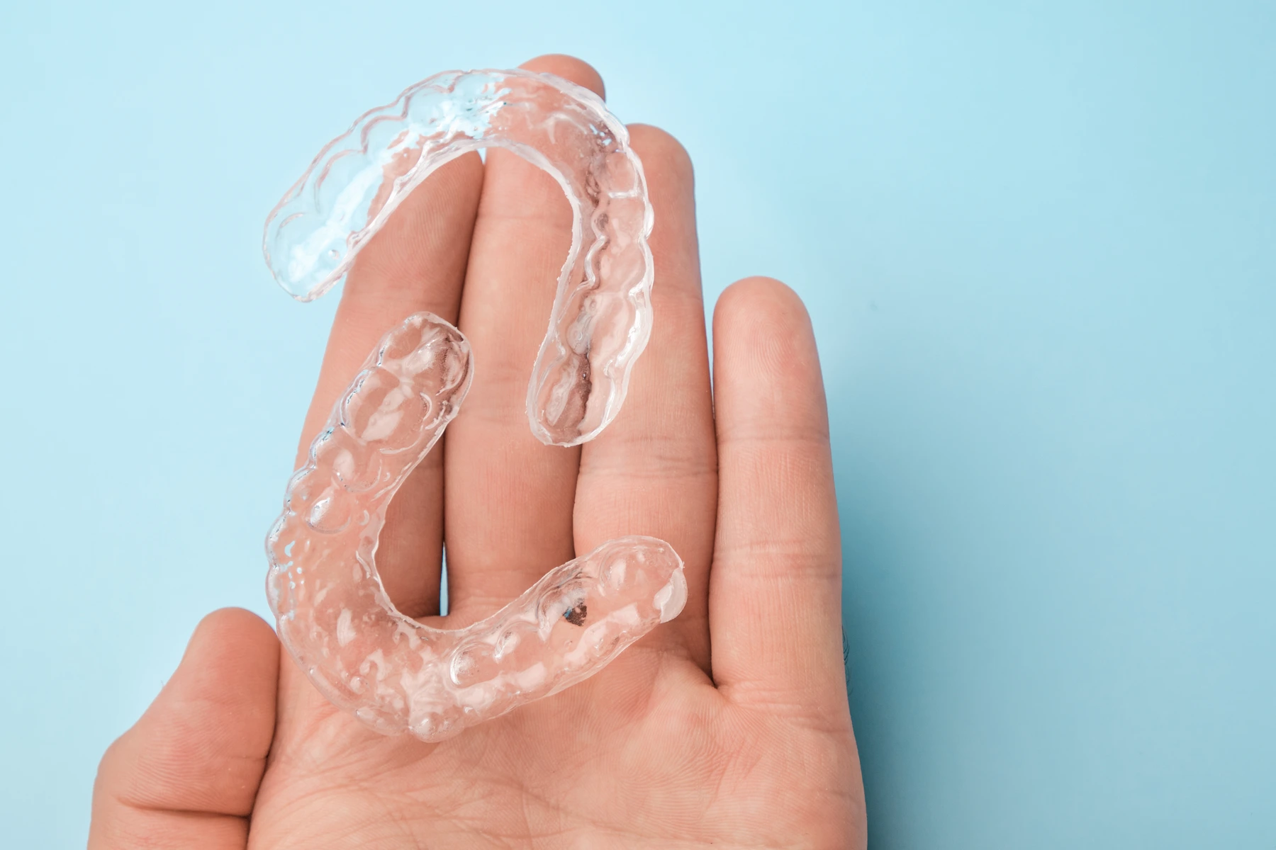 hand holding a pair of invisalign tray with a light background
